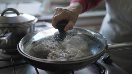 Close-Up View of a Hand Adjusting the Lid on a Sizzling Pan, Cooking Process in Action