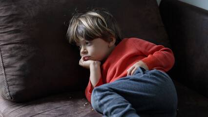 Contemplative Young Boy Lying on a Dark Brown Sofa in a Relaxed Pose