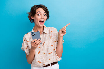 Photo of charming astonished person hold smart phone direct finger empty space isolated on blue...