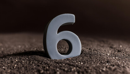 Number 6 made of gray stone isolated with shadow over dark sand.