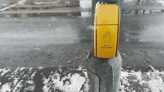 Tourist man press pedestrian traffic light button in Cologne, Germany, during a snowy day with blurred street background.