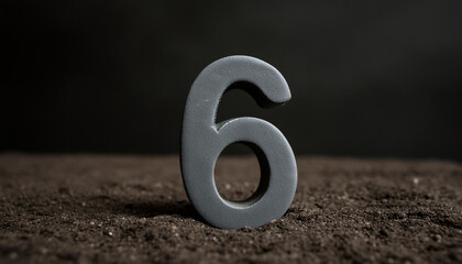 Number 6 made of gray stone isolated with shadow over dark sand.