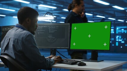 Programmer coding on isolated screen computer in data center, supervising server rows in computer...