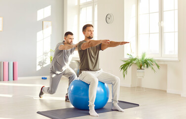 Male caregiver or doctor physiotherapist helping young man doing sport exercises sitting on fit...