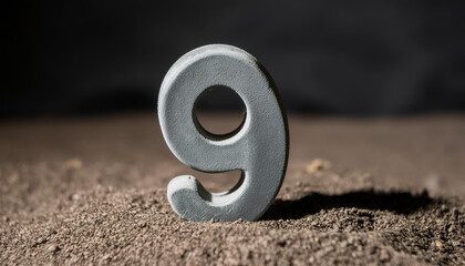 Number 9 made of gray stone isolated with shadow over dark sand.