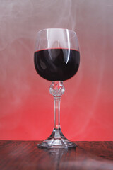 A beautiful glass of red wine surrounded by smoke. Glass with wine on a wooden surface.