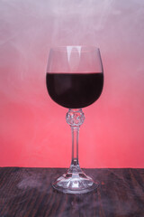 A beautiful glass of red wine surrounded by smoke. Glass with wine on a wooden surface.