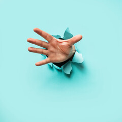 Hand Bursting through Blue Paper