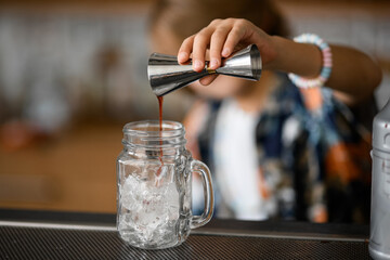 Small boy pours brown syrup from a jigger into a handle jar filled with ice