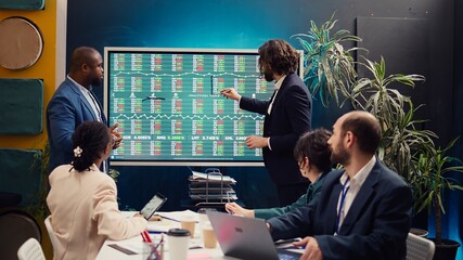 Team of business analysts following stock trade trends on interactive board, developing a new...