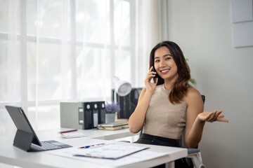 Obraz premium A woman is talking on her cell phone while sitting at a desk