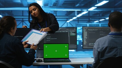 Green screen laptop in data center in front of manager and IT support specialists working together,...