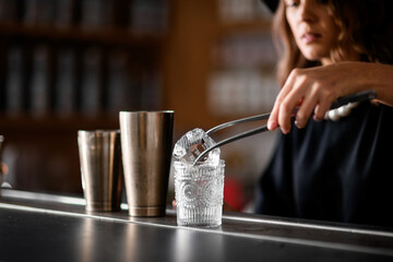 Female bartender puts a huge ice cube into a glass with tweezers