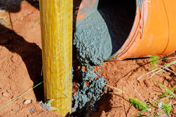 Pouring concrete over newly installed timber fencing wooden fence posts