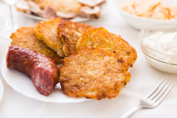 Potato pancakes with fried sausage on white plate