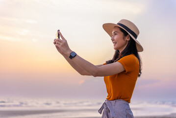 Asian woman using smartphone taking a photo with attractive smile at beach. Happy Asian woman for tropical travel holidays. People with travel and holiday concept. Slow motion concept.