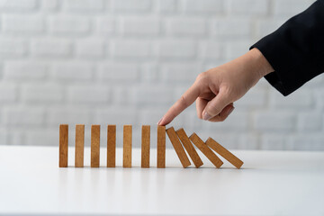 Photograph of business woman's hands stopping falling wooden dominoes Financial hedging concept.