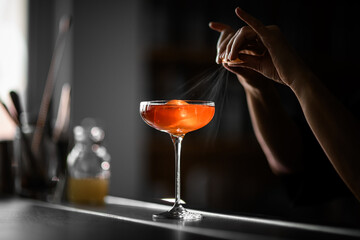Female hands squeeze a piece of zest that splashes over a glass with a cocktail