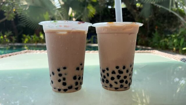 Milk bubble tea with tapioca pearls in glass, gray background. Two Bubble Tea drinks with ice and Tapioca topical balls, a large straw, stir and pierce