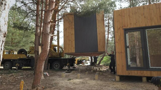 Crane Lifting Modern Prefab Cabin Into Place in Wooded Area