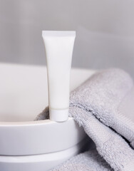 White cosmetic tube on vessel sink near grey folded towels in bathroom close up, mockup