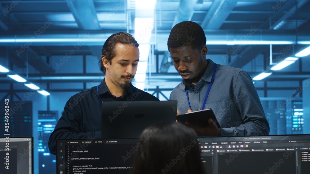 Poster multiethnic coworkers in server room collaborating to fix servers providing computing resources for 