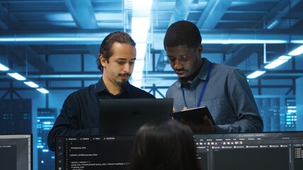 Multiethnic coworkers in server room collaborating to fix servers providing computing resources for...