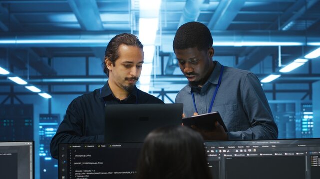 Multiethnic coworkers in server room collaborating to fix servers providing computing resources for workloads. Diverse team of admins supervising data center supercomputers - Powered by Adobe
