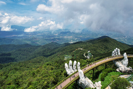 A statue holds a bridge over a river with a scenic landscape Vietnam Da Nang Ba Na Hills Asia