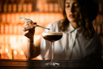 Tall glass with a brown cocktail with foam stands on the bar counter