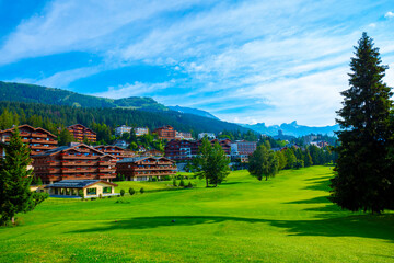 Village with House and Hotel with Panoramic View over Mountain with Clouds and Golf Course in a Sunny Summer Day in Crans Montana, Valais, Switzerland.