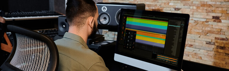 A man, part of a music band, sits at a computer in a recording studio, overseeing the rehearsal process.