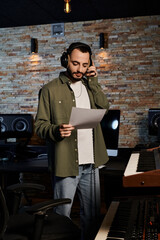 A man in headphones stands confidently in front of a recording studio, ready for a music band...
