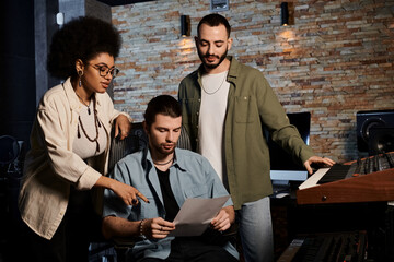 Three individuals in a recording studio scrutinizing a sheet of music.