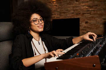 Female with afro hair energetically playing a keyboard in a recording studio during a music band...