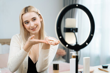 Young woman making beauty and cosmetic tutorial video content for social media. Beauty blogger smiles to camera while showing how to apply beauty skincare to audience or followers. Blithe