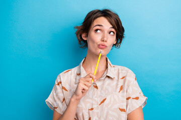 Photo of creative pensive lady hold pencil touch chin look interested empty space isolated on blue...