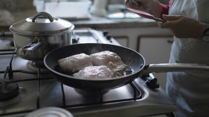 Senior Woman Cooking Fish in a Pan - Home Kitchen Scene with Steam Rising