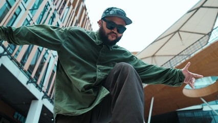 Low angle view of hipster pose in hip hop style surrounded by mall view. Portrait of sporty asian hip hop choreographer dancing break dance while looking at camera. Outdoor sport 2024. Endeavor.