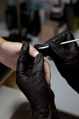 Fototapeta premium A detailed view of a manicurist’s hands in black gloves, using a wooden stick to clean a client’s nails, emphasizing the precision and care in nail treatment.