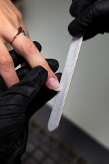 Close-up of a manicurist using a nail file to shape a client’s nails, highlighting the meticulous...