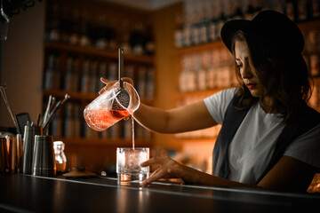 Female bartender pours a brown cocktail into a cocktail glass