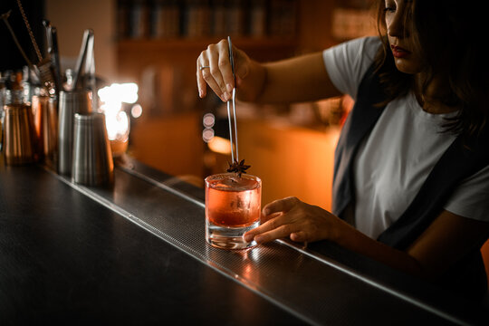 Female bartender decorates pink cocktail with ice with vanilla flower