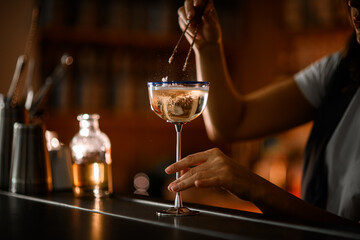 Female hands of a bartender drowned a piece of cotton candy in a glass on a tall metal leg