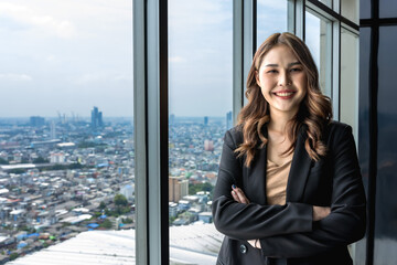 Fototapeta premium portrait of young Asian business woman standing arm crossed in high rise office in downtown Bangkok