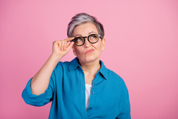 Photo of lovely pensioner lady look skeptical empty space touch specs dressed stylish blue garment isolated on pink color background