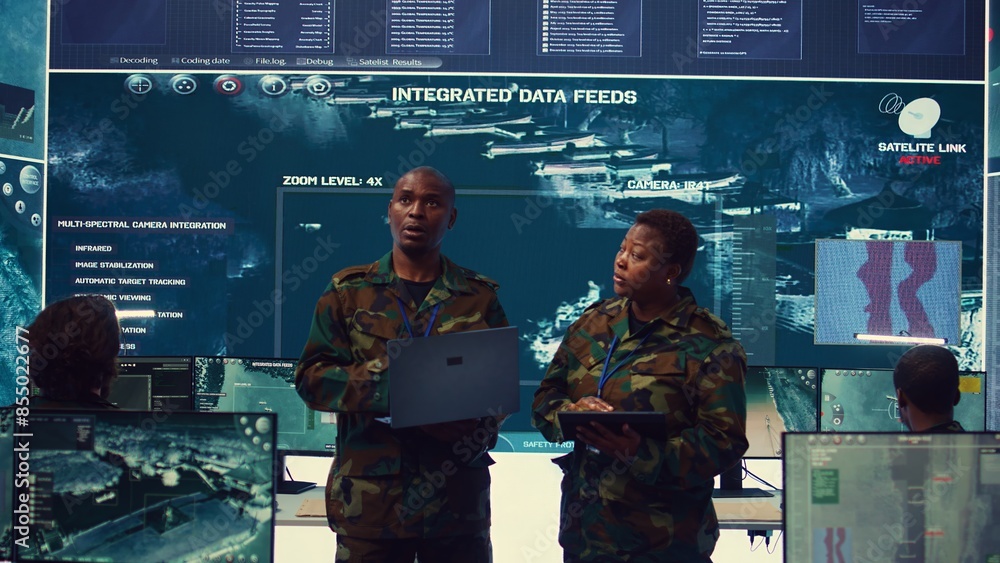 Poster sergeant major and female soldier checking real time field data in command post monitoring room, exa