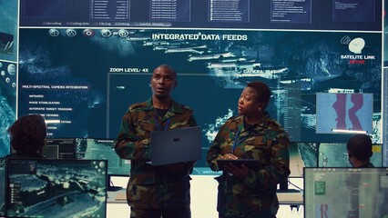 Sergeant major and female soldier checking real time field data in command post monitoring room,...