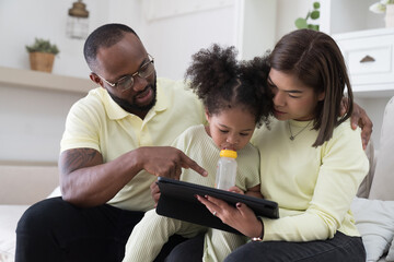 Father, mother and little daughter playing digital tablet together during daughter eating milk from nipples bottle at home