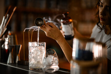 Female bartender pours a clear drink from a jigger into a mixing glass filled with ice